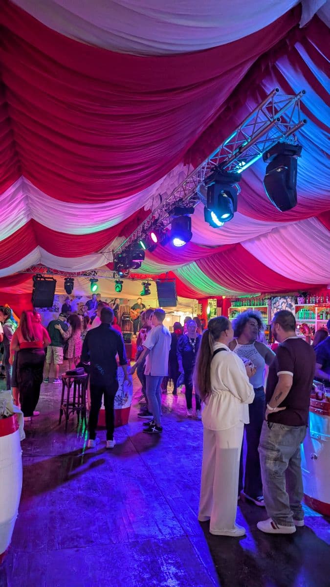 Feria de San Pedro 2025, 15 oct — pista de baile en caseta con carpa roja y blanca y luces de escenario, San Pedro Alcántara, Marbella
