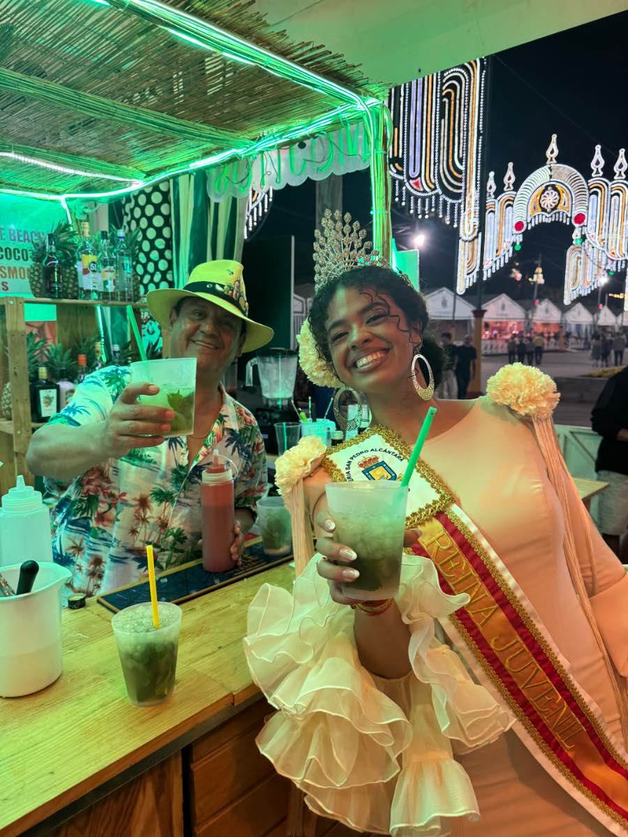 Feria de San Pedro Alcántara 2025, 15 oct — dama de honor con mojito en barra de caseta bajo luces del recinto ferial La Caridad, Marbella.